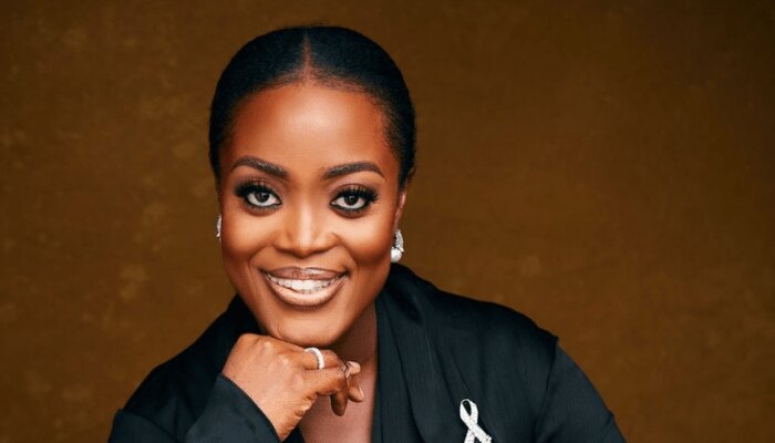 Studio portrait of Dr. Adaeze Oreh in black with a white awareness ribbon, against a warm gold backdrop.